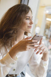 Portrait of young woman holding cell phone in a cafe - FMOF00758