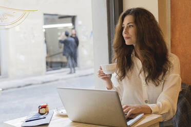 Junge Frau mit Laptop in einem Cafe - FMOF00763