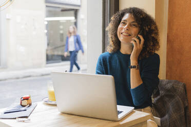 Happy woman using smartphone and laptop in a cafe - FMOF00765