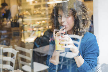 Porträt einer Frau, die einen Smoothie hinter einer Fensterscheibe in einem Café trinkt - FMOF00769