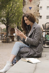 Junge Frau mit Smartphone und Kopfhörern im Freien in der Stadt - FMOF00782