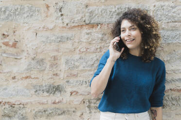 Lächelnde Frau am Telefon vor einer Steinmauer - FMOF00790