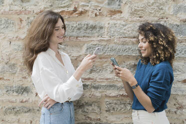 Zwei Frauen benutzen Smartphones im Freien - FMOF00792