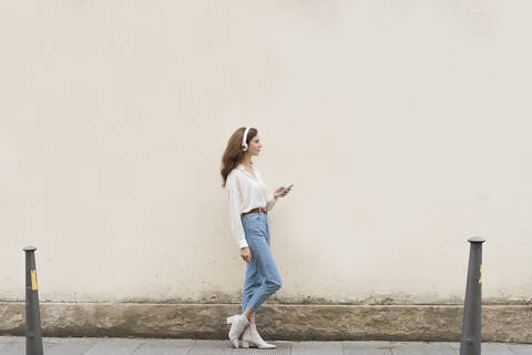 Junge Frau mit Smartphone und Kopfhörern auf dem Gehweg, lizenzfreies Stockfoto