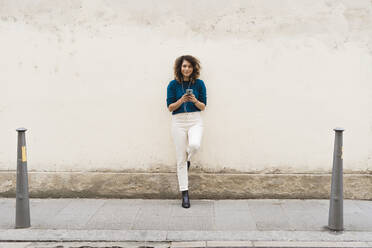 Smiling woman with smartphone and earphones on sidewalk - FMOF00802