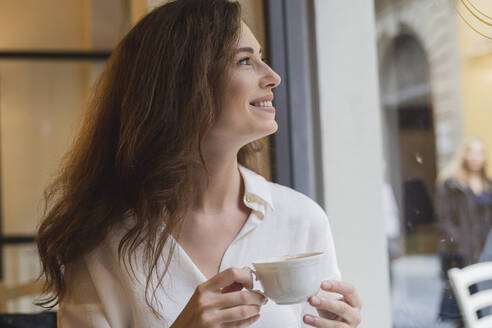 Happy young woman looking out of window in a cafe - FMOF00806