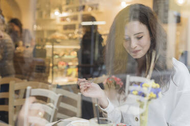 Lächelnde junge Frau isst Kuchen in einem Cafe - FMOF00810