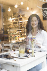 Porträt einer lächelnden jungen Frau hinter einer Fensterscheibe in einem Cafe - FMOF00811