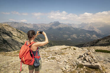 Wanderin während einer Wanderung, fotografierend mit ihrem Aussichtspunkt, Haute-Corse, Korsika, Frankreich - MSUF00050