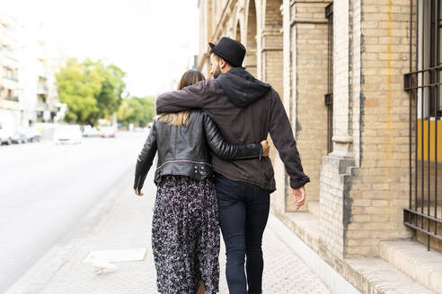 Rückansicht eines jungen verliebten Paares, das Arm in Arm durch die Stadt läuft - ERRF02148