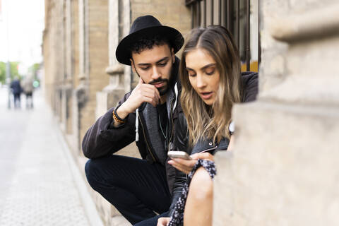 Junges Paar sitzt im Freien und schaut auf sein Handy, lizenzfreies Stockfoto