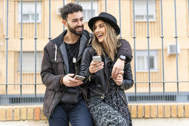 Portrait of laughing young couple with their mobile phones in the city - ERRF02167