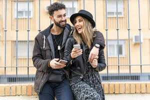 Porträt eines lachenden jungen Paares mit ihren Handys in der Stadt - ERRF02167