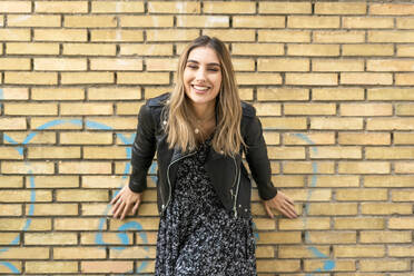 Porträt einer lachenden jungen Frau vor einer Backsteinmauer - ERRF02173