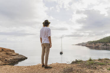 Rückenansicht eines jungen Mannes, der vor dem Meer steht und die Aussicht betrachtet, Ibiza, Balearische Inseln, Spanien - AFVF04248