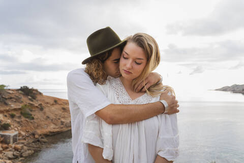 Junges verliebtes Paar vor dem Meer stehend, Ibiza, Balearische Inseln, Spanien, lizenzfreies Stockfoto