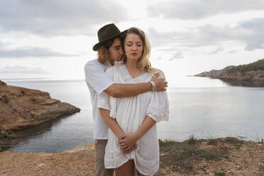 Porträt eines jungen verliebten Paares, das mit geschlossenen Augen vor dem Meer steht, Ibiza, Balearische Inseln, Spanien - AFVF04259
