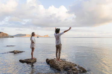 Junges Paar steht auf Felsen vor dem Meer, Ibiza, Balearen, Spanien - AFVF04279