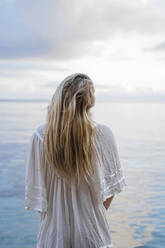 Back view of young blond woman standing in front of the sea, Ibiza, Balearic Islands, Spain - AFVF04287