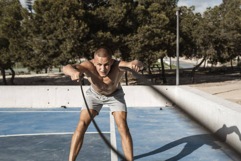 Barechested muscular man exercising with battle ropes outdoors - RCPF00141