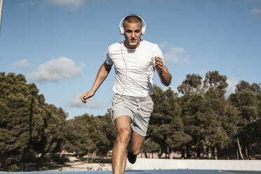 Young man with headphones running outdoors - RCPF00148