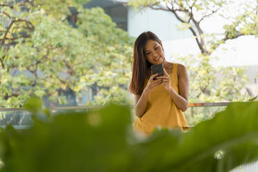 Porträt einer lächelnden, gelb gekleideten Frau mit Smartphone auf einer Terrasse - MAUF03106