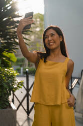 Porträt einer modisch gekleideten Frau in Gelb, die ein Selfie mit ihrem Smartphone macht - MAUF03133