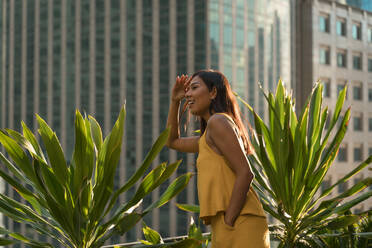 Smiling woman standing on roof terrace looking at distance, Bangkok, Thailand - MAUF03140