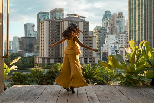 Back view of woman dancing on roof terrace, Bangkok, Thailand - MAUF03142