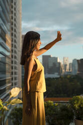 Frau steht auf einer Dachterrasse und beobachtet den Sonnenuntergang, Bangkok, Thailand - MAUF03143