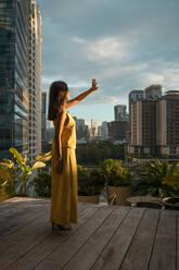 Frau auf Dachterrasse im Sonnenlicht, Bangkok, Thailand - MAUF03144