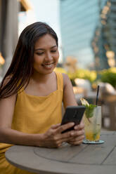 Porträt einer lächelnden Frau, die in einem Café sitzt und auf ihr Mobiltelefon schaut - MAUF03149