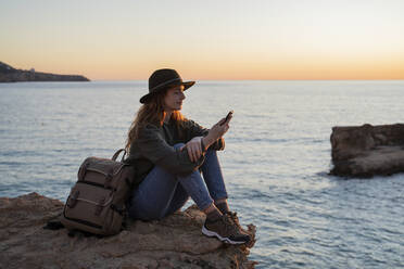 Junge Frau benutzt Smartphone am Strand bei Sonnenuntergang, Ibiza - AFVF04289