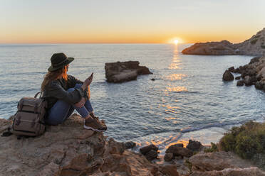 Junge Frau benutzt Smartphone am Strand bei Sonnenuntergang, Ibiza - AFVF04290