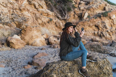 Junge Frau benutzt Smartphone am Strand bei Sonnenuntergang, Ibiza - AFVF04294