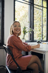 Porträt einer lächelnden Geschäftsfrau, die sich am Schreibtisch im Büro Notizen macht - ZEDF02707