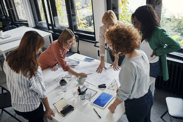 Businesswomen having a meeting in office with blueprints on table - ZEDF02760