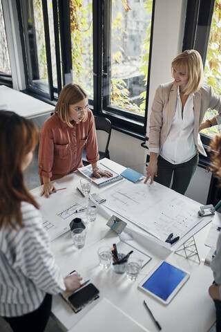 Geschäftsfrauen mit einer Sitzung im Büro mit Blaupausen auf dem Tisch, lizenzfreies Stockfoto