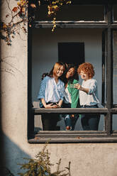 Three businesswomen standing at the window of an office building taking a selfie - ZEDF02771