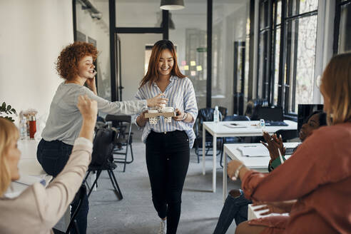 Businesswoman serving coffee to colleagues in office - ZEDF02772