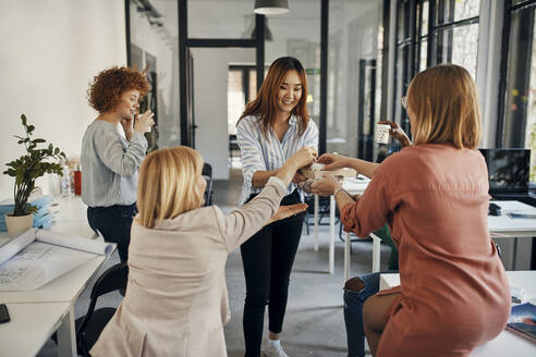 Businesswoman serving coffee to colleagues in office - ZEDF02774