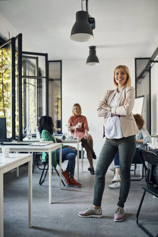 Portrait of confident pregnant businesswoman in office with colleagues in background stock photo