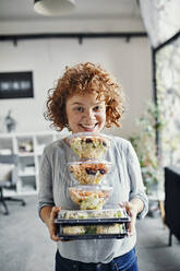 Porträt einer lächelnden Geschäftsfrau mit einem Stapel Essen zum Mitnehmen im Büro - ZEDF02793