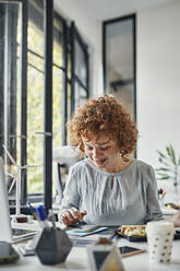 Businesswoman using smartphone during lunch break in office - ZEDF02801