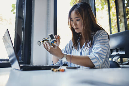 Businesswoman holding model car at desk in office - ZEDF02802