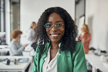 Portrait of a smiling businesswoman in office with colleagues in background - ZEDF02809