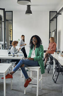 Portrait of a smiling businesswoman sitting on stool in office - ZEDF02811