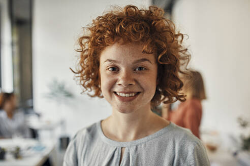Portrait of a smiling redheaded businesswoman in office - ZEDF02820