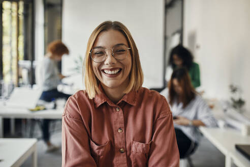 Portrait of a happy businesswoman in office with colleagues in background - ZEDF02825