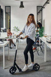 Porträt einer Geschäftsfrau mit Kick-Scooter im Büro - ZEDF02828